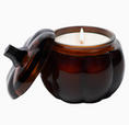 Load image into Gallery viewer, An amber glass jar candle with a matching lid leaning against it, shown on a plain light gray background. The candle is open, revealing white wax and a single lit wick.