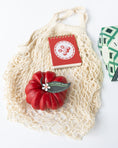 Load image into Gallery viewer, An angled view of a Farmer's Market-themed gift with a mesh net bag, a tomato-shaped red candle, a red mini notebook with a tomato graphic on top, and a box of Maldon salt just out of frame.