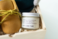 Load image into Gallery viewer, A jar of Little Seed Farm Booty Balm placed in a wooden gift box with shredded paper, next to a tan suede bootie with a yellow-green laces, against a light gray background.