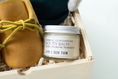 Load image into Gallery viewer, A jar of Little Seed Farm Booty Balm placed in a wooden gift box with shredded paper, next to a tan suede bootie with a yellow-green laces, against a light gray background.