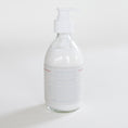 Load image into Gallery viewer, A clear glass pump bottle filled with white lotion, featuring a white pump dispenser and a white label with fine blue text and thin red lines, set against a plain white background.