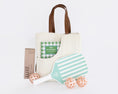 Load image into Gallery viewer, A cream canvas pickleball bag with brown leather handles, styled with a mint green and white striped pickleball paddle, three peach-orange pickleballs, a brown pickleball package labeled LUXE, and a green-and-white checkered pickleball book in its front pocket, all on a white background.