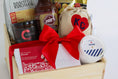 Load image into Gallery viewer, A wooden gift basket filled with assorted food items including a bag of Topsy's Popcorn KC Mix, a package of The Roasterie Coffee, a jar of Cocoavino, Joe's BBQ Sauce, a KC Heart Candle displayed in and outside of the candle pouch, and Andre's chocolates, tied with a red ribbon on a white background.
