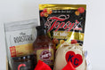 Load image into Gallery viewer, A wooden gift basket filled with assorted food items including a bag of Topsy's Popcorn KC Mix, a package of The Roasterie Coffee, a jar of Cocoavino, Joe's BBQ Sauce, a KC Heart Candle displayed in and outside of the candle pouch, and Andre's chocolates, tied with a red ribbon on a white background.