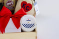 Load image into Gallery viewer, A wooden gift basket filled with assorted food items including a bag of Topsy's Popcorn KC Mix, a package of The Roasterie Coffee, a jar of Cocoavino, Joe's BBQ Sauce, a KC Heart Candle displayed in and outside of the candle pouch, and Andre's chocolates, tied with a red ribbon on a white background.