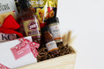 Load image into Gallery viewer, A wooden gift basket filled with coffee and tea items, including Andre's Chocolates, a bag of Topsy's Popcorn KC Mix, Roasterie Coffee, Joe's BBQ Sauce, and Jack Stack mini seasoning and bbq sauce set, arranged in a light wood crate with a red ribbon on a white background.