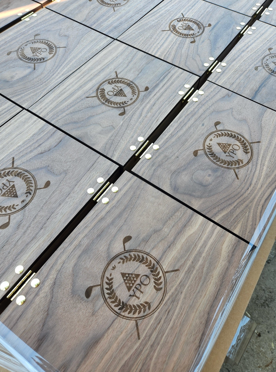 An overhead shot of multiple dark wood gift boxes, engraved with golf-themed logos and featuring metal hardware.