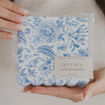 Load image into Gallery viewer, A person holds a packaged set of scalloped cocktail napkins with a blue floral toile pattern on a white background. The napkins are in clear plastic packaging with a paper label that reads 'SWEET WATER DECOR DELFT BLUE cocktail napkins'.
