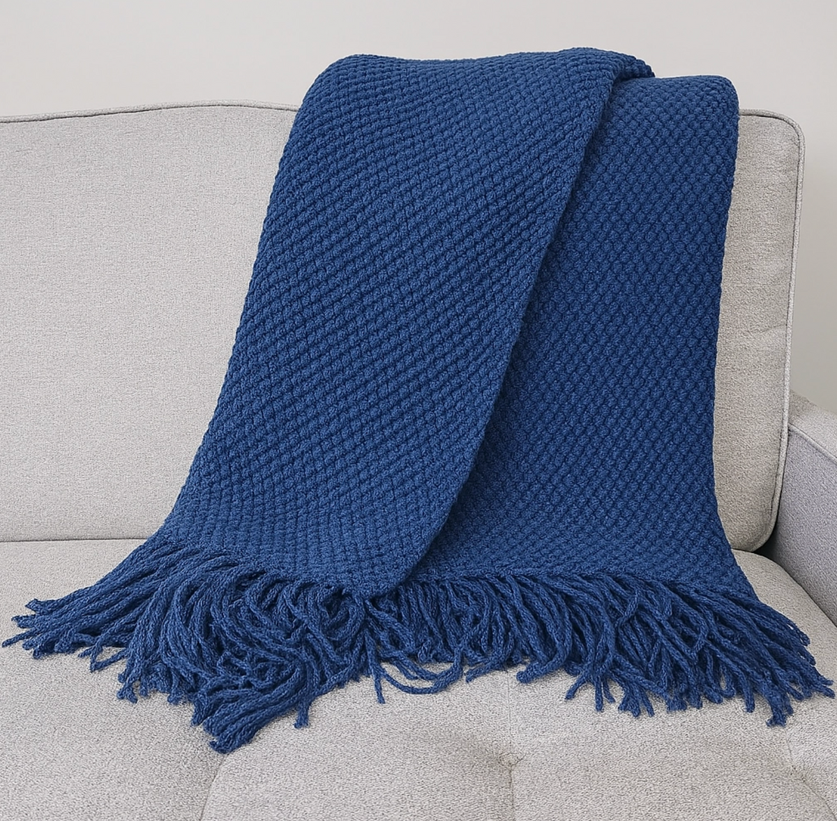A textured navy blue throw blanket with fringe, draped over a light gray upholstered armchair.