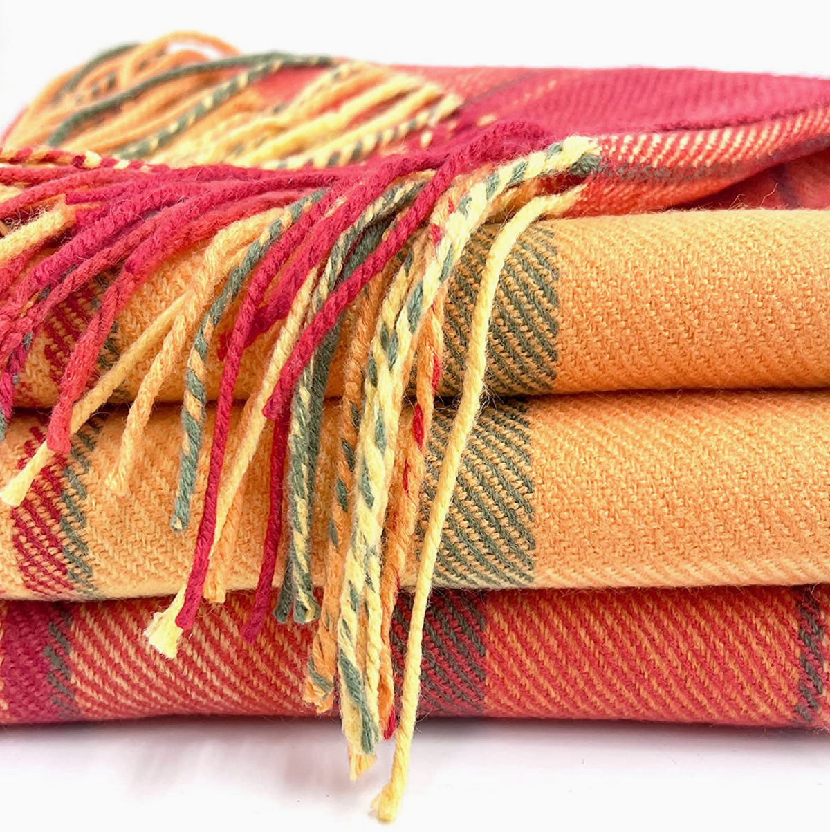A stack of folded plaid blankets in warm autumn colors, including orange, red, yellow, and green, with fringed edges visible against a white background.