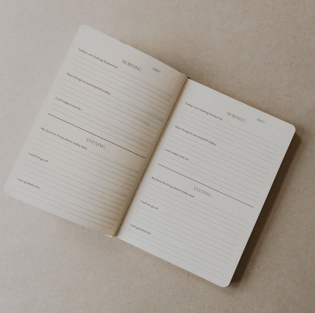An open minimalist daily planner notebook on a textured beige background, showing lined pages with sections for morning and evening activities.