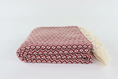 Load image into Gallery viewer, A folded woven turkish linen with a red and white geometric pattern and cream tassels on one end, photographed on a clean white background.
