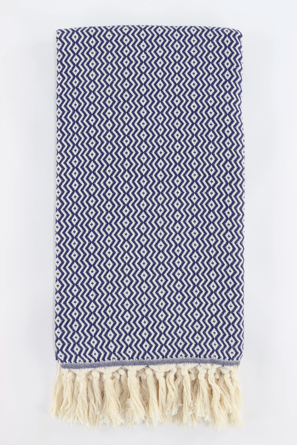 A folded woven turkish towel with a blue and white geometric zigzag pattern and cream fringe tassels along one edge, shown on a plain white background.