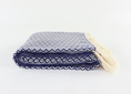 Load image into Gallery viewer, A folded woven turkish towel with cream tassels, featuring a navy blue and off-white geometric pattern on a plain white background.
