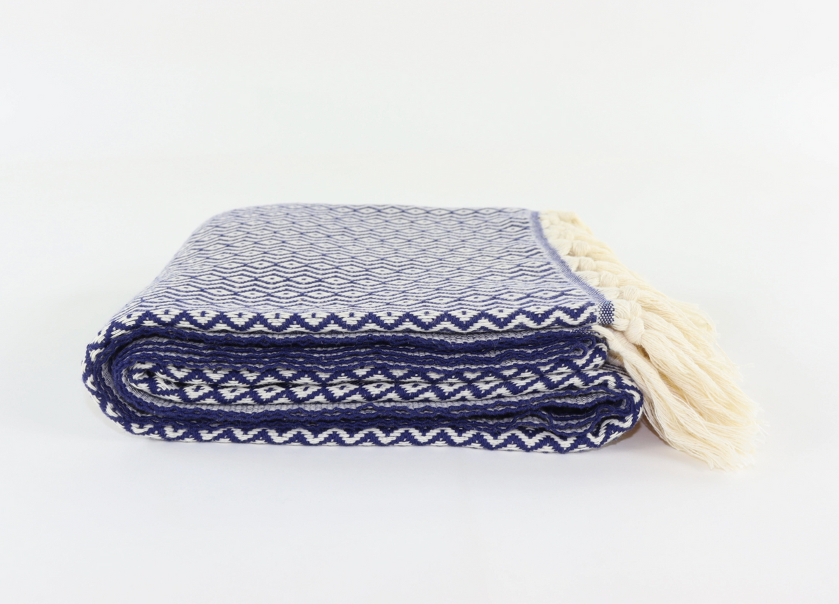 A folded woven turkish towel with cream tassels, featuring a navy blue and off-white geometric pattern on a plain white background.