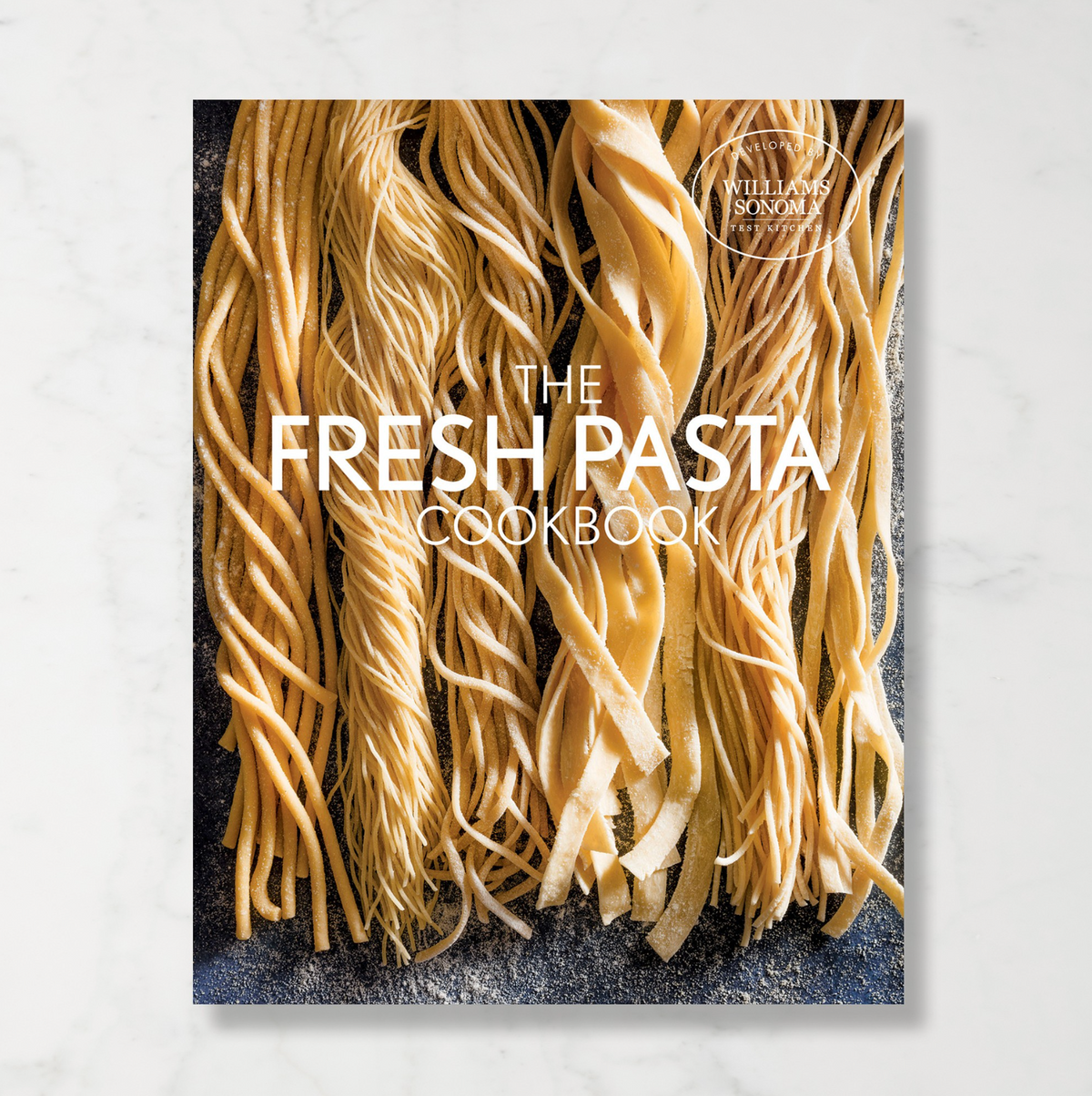 Williams Sonoma cookbook called The Fresh Pasta Cookbook with an image of different handmade long noodles dusted in flour on the front cover.