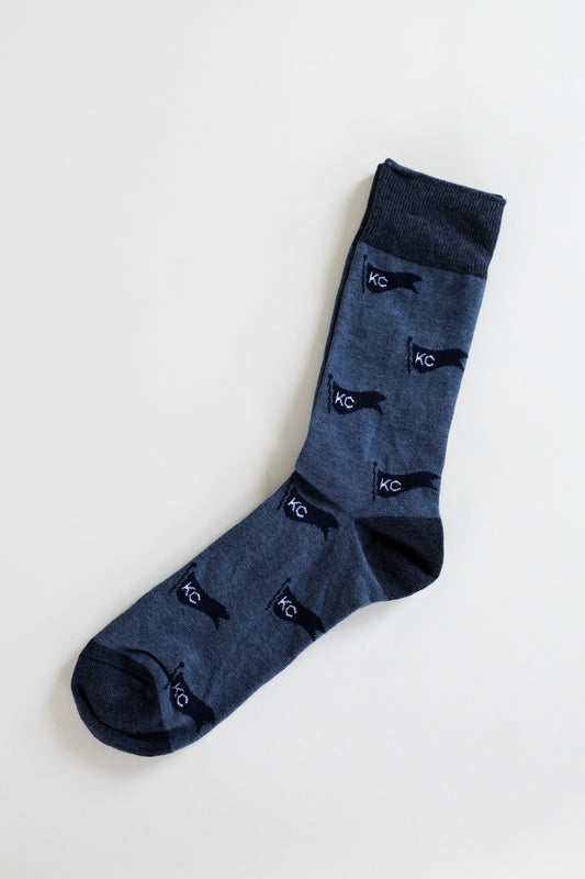 A pair of dark blue crew socks with a repeating pattern of navy blue silhouette pennant flags and white 'KC' initials, displayed on a clean off-white background.