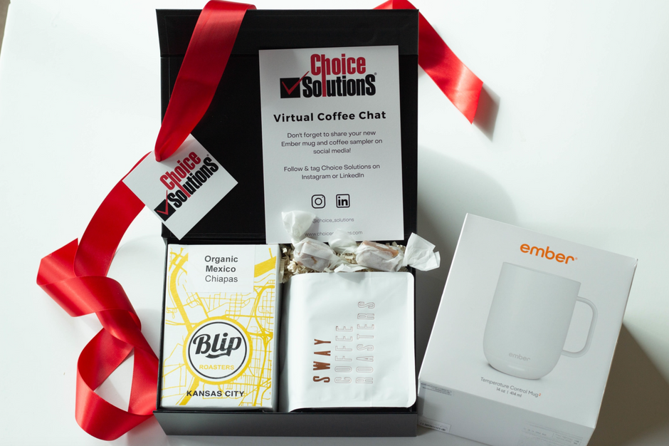 A curated gift box set on a white background featuring a black Choice Solutions branded box with a red ribbon, a blue and yellow Blip Kansas City coffee bag, a white coffee bag from Sway Roasters, and an Ember mug.