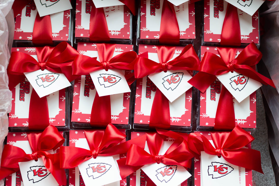 A grid of small gift boxes tied with bright red satin bows and white tags featuring the Kansas City Chiefs logo, arranged closely together.