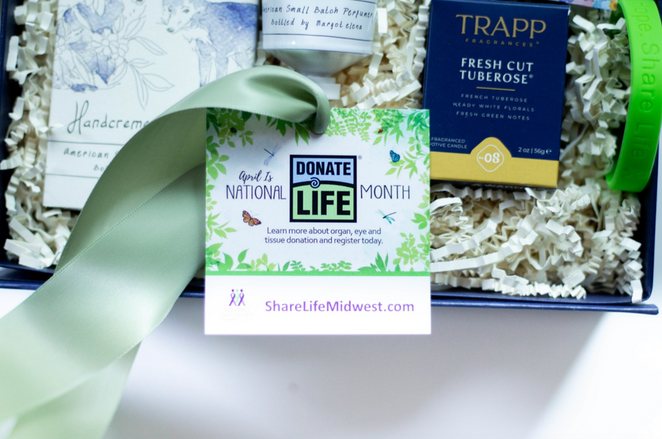 A curated gift box containing a Trapp Fresh Cut Tuberose candle box, a hand cream bottle, and a central 'Donate to National Life' card tied with a pale green ribbon, arranged in white crinkle paper.