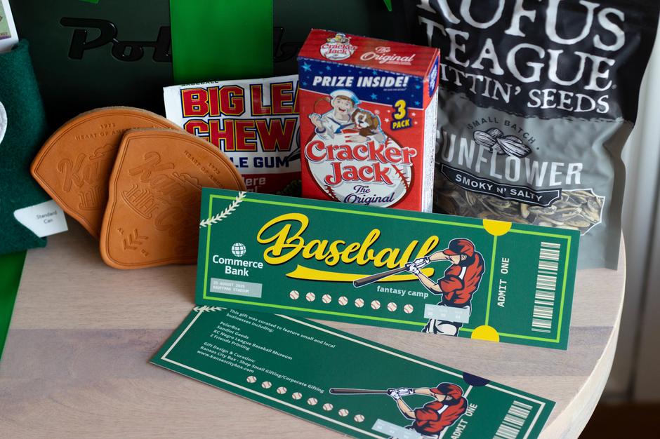 A tabletop display of themed novelty baseball items, including a green and yellow 'Baseball' ticket, two custom engraved brown leather coasters, a red 'Cracker Jack' box, and a black bag of sunflower seeds with 'Rufus Teague' branding.