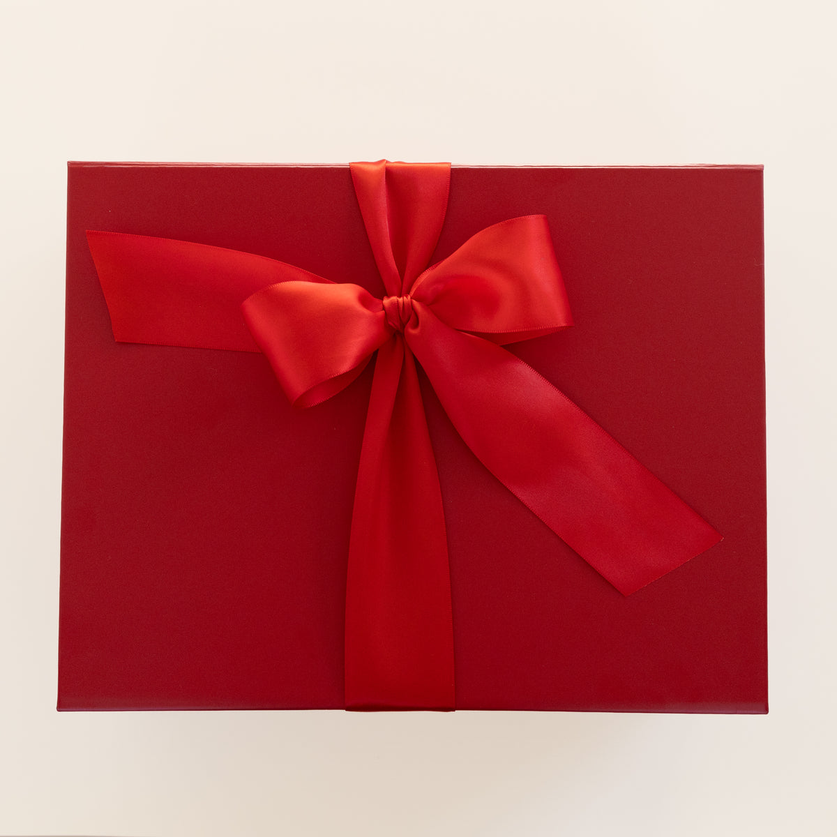 A red gift box wrapped with a wide red satin ribbon tied in a large bow, photographed from above on a plain light background.