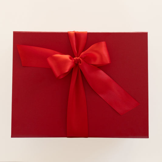 A red gift box wrapped with a wide red satin ribbon tied in a large bow, photographed from above on a plain light background.