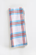 Load image into Gallery viewer, A folded kitchen towel with a white waffle-weave texture, featuring a plaid pattern of light blue, orange, and thin red stripes, set against a plain white background.

