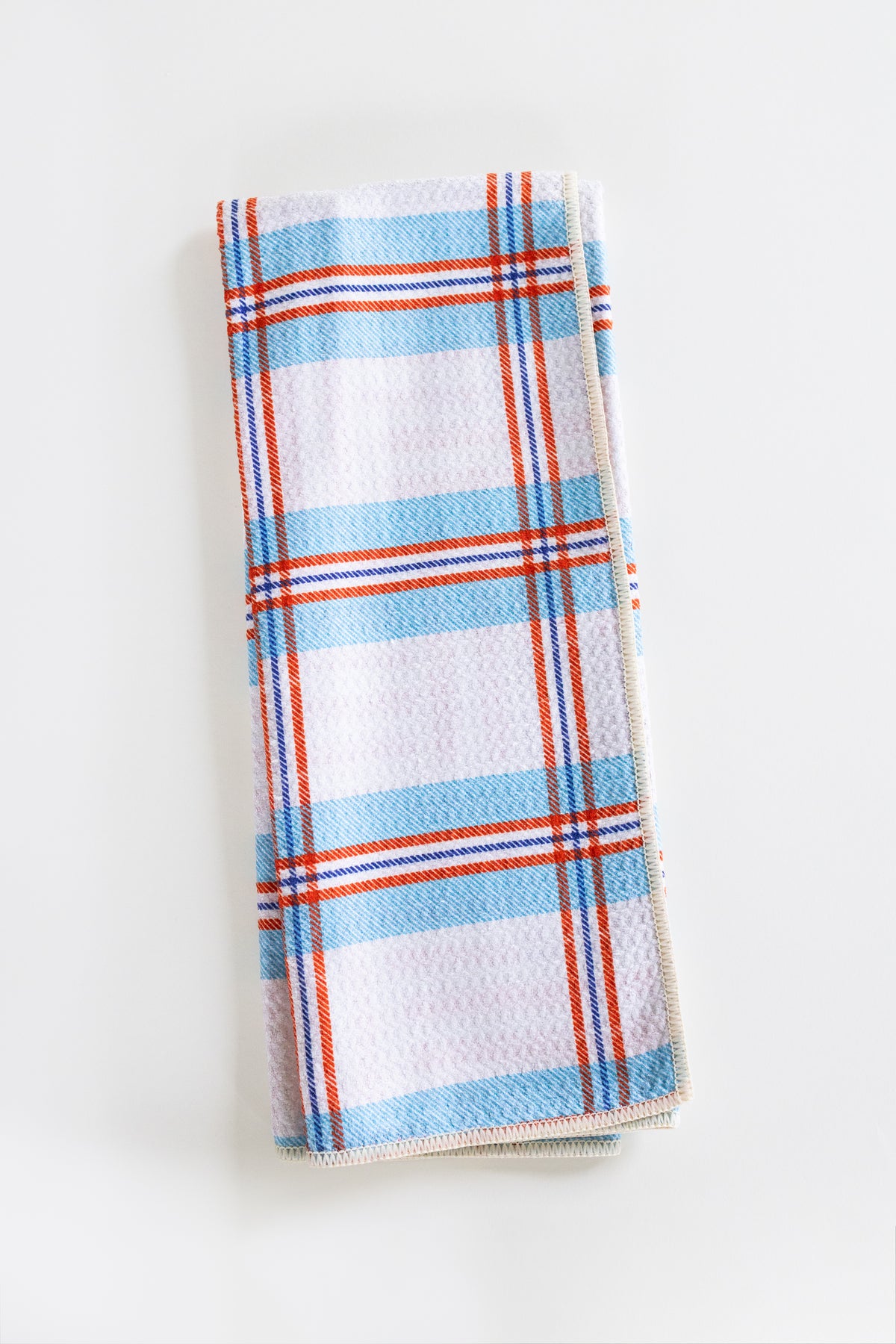 A folded kitchen towel with a white waffle-weave texture, featuring a plaid pattern of light blue, orange, and thin red stripes, set against a plain white background.