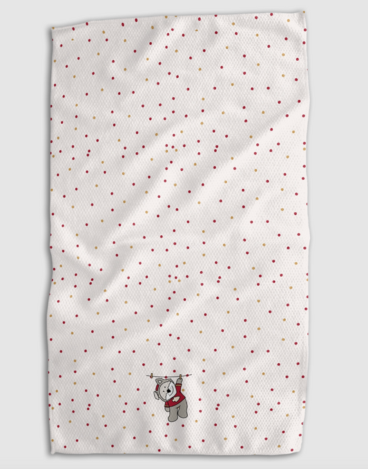 A white textured tea towel with a scattered pattern of small red and gold dots, featuring a small gray wolf plushie wearing a red sweater near the bottom center, shown against a neutral gray background.