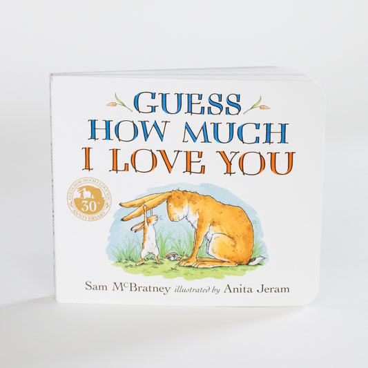 A children's board book titled 'Guess How Much I Love You' by Sam McBratney, illustrated by Anita Jeram. The book features a white cover with blue and orange lettering and an illustration of a large rabbit and a small rabbit in grass.