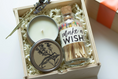 Load image into Gallery viewer, A birthday gift set in a light wood box filled with white paper shred, featuring a white candle in a silver tin with a botanical bird illustration., and a small glass bottle of matches labeled 'make a WISH!' with a cork stopper.
