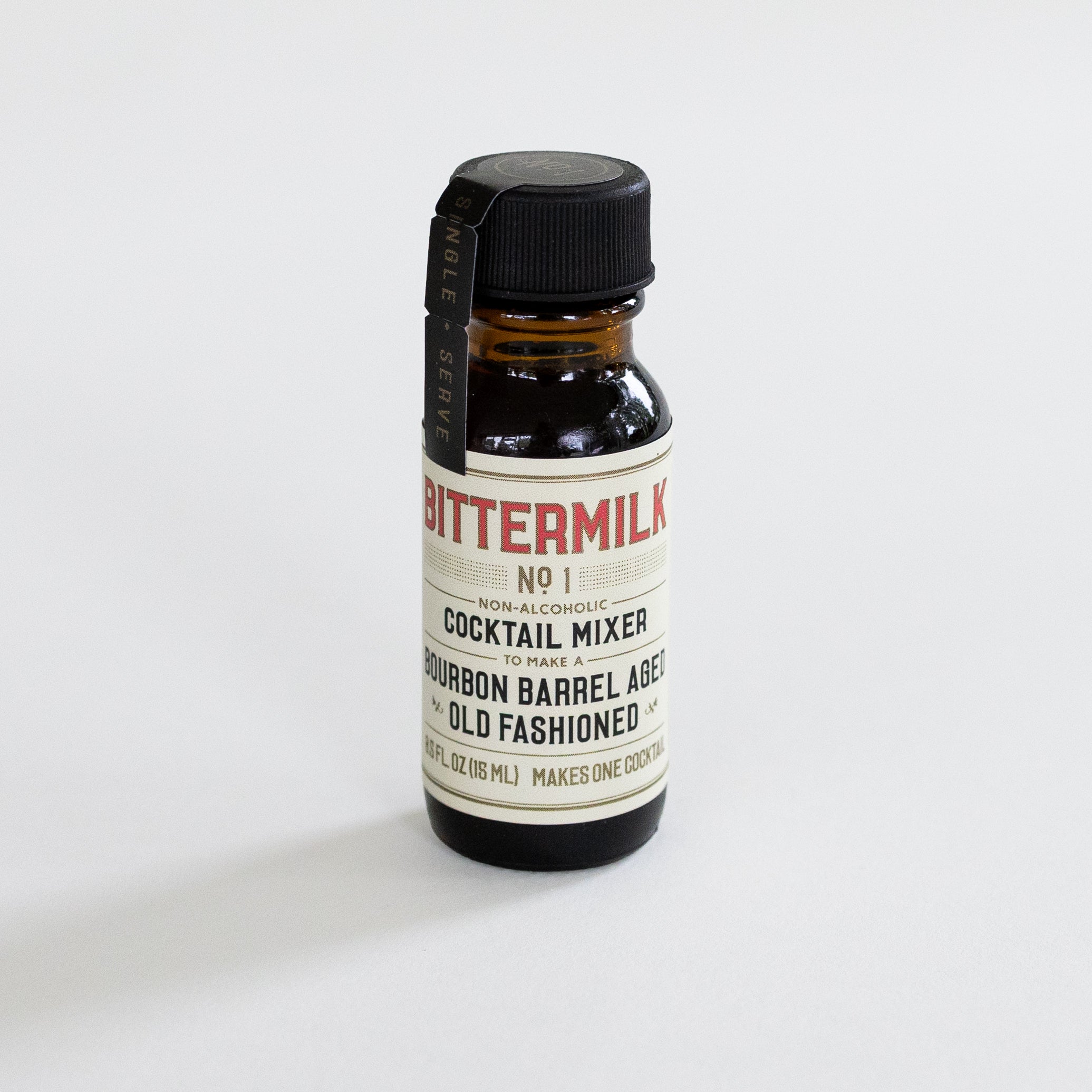 A small amber glass bottle of Bitter Milk No. 1 Cocktail Mixer with a black cap and cream label, photographed on a clean white background.