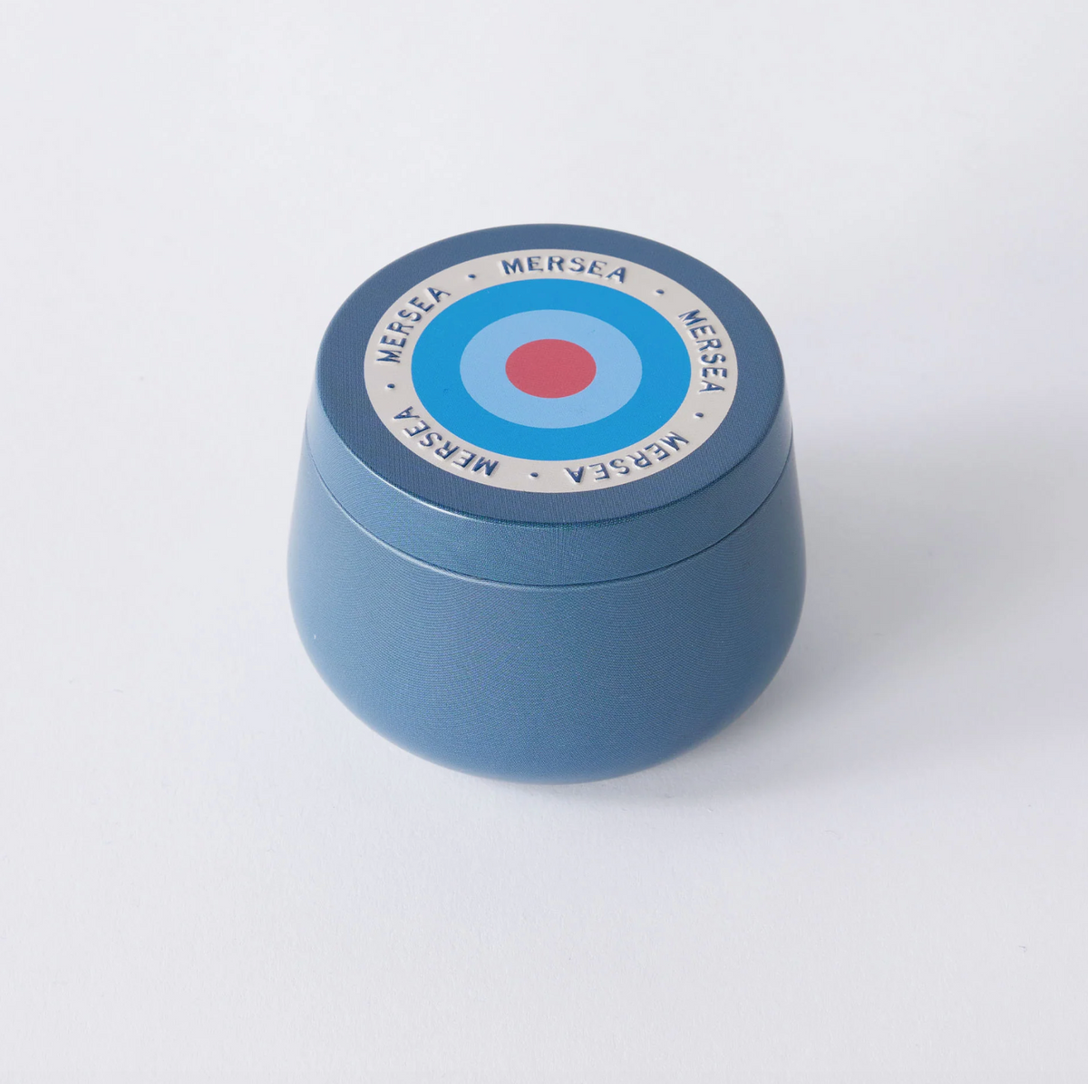 A round blue cosmetic jar with a matching lid, featuring a circular target design in blue, white, and red with the brand name 'MERSEA' printed around the target.