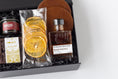 Load image into Gallery viewer, A curated gift box set in a black presentation box with shredded black filler, featuring a jar of cocktail cherries, a bag of California Crisps dried orange slices, a bottle of Strongwater Black Walnut cocktail bitters, a package of Andre's Bourbon Balls, and two brown leather coasters.
