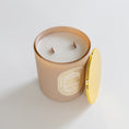 Load image into Gallery viewer, A candle in a frosted beige glass jar with a gold label reading 'COCO CLOUD', shown with its gold lid leaning against it on a clean white background.
