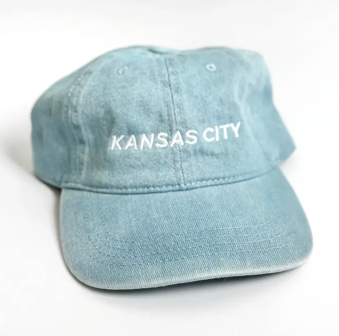 A light blue washed cotton baseball cap with 'KANSAS CITY' embroidered in white on the front, shown on a plain white background.