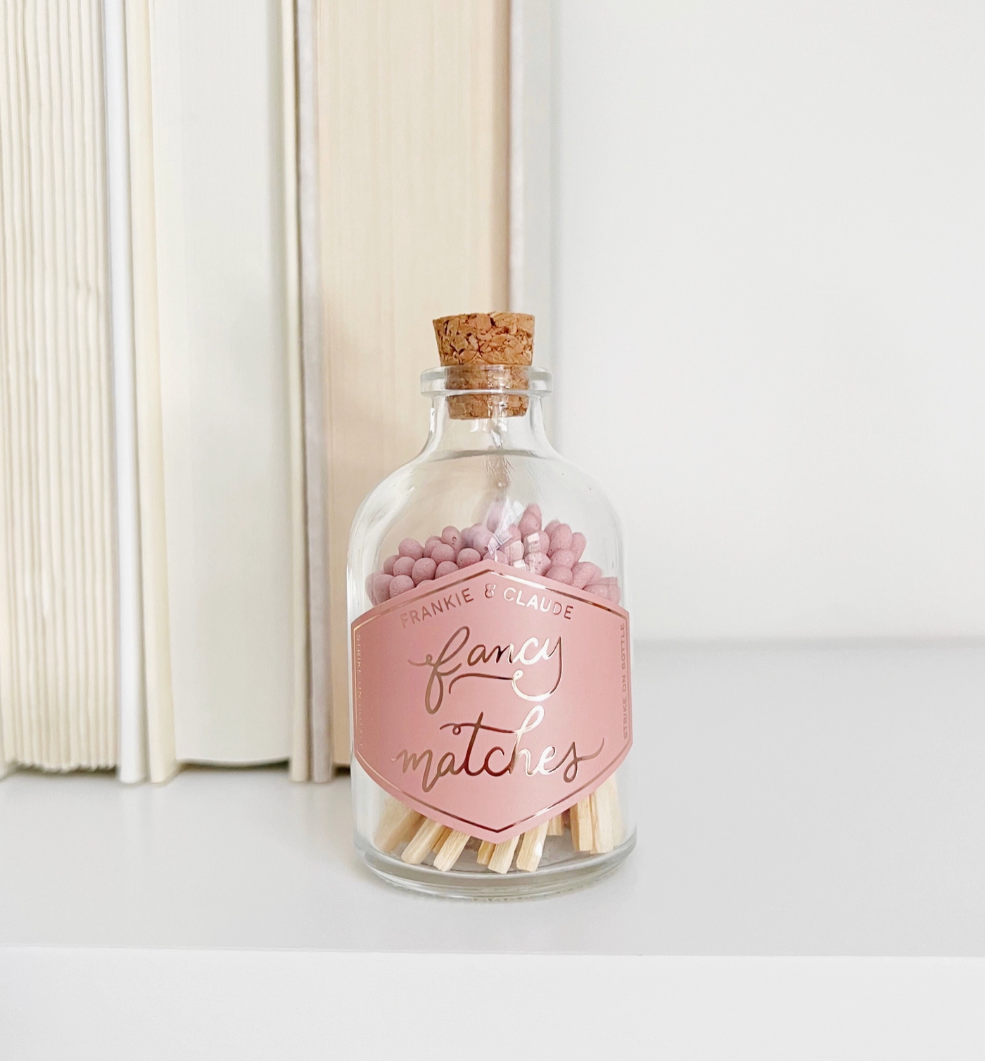 a glass jar of pink-tipped matches on a bookshelf ledge. The label on the glass jar reads "Fancy Matches"
