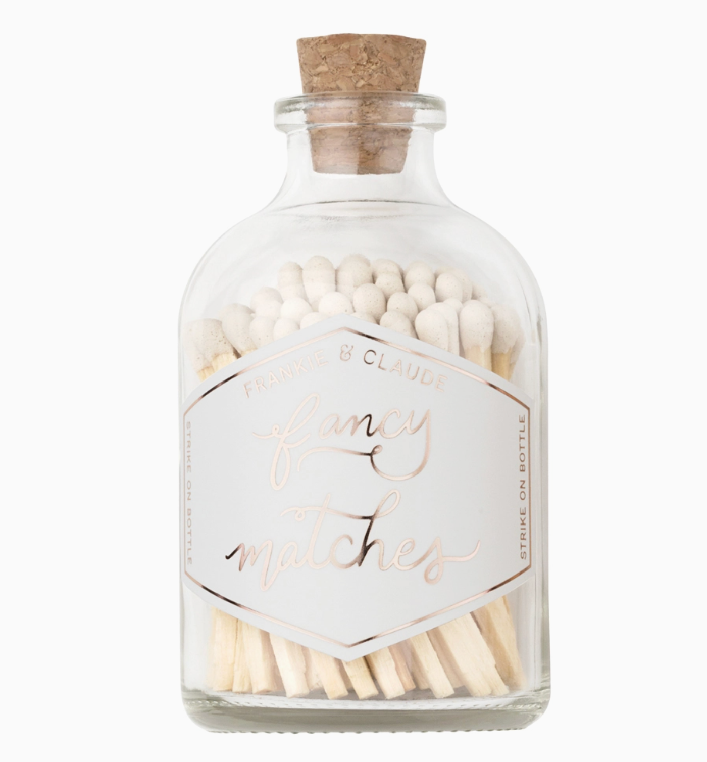 A clear glass bottle with a cork stopper filled with matchsticks, featuring a white label with metallic rose-gold foil text that reads 'Fancy Matches' and 'Frankie & Claude'.