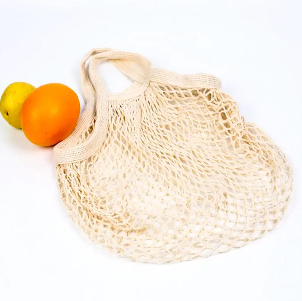 A natural cream-colored cotton mesh reusable bag with woven handles, shown on a white background with an orange and a yellow fruit partially tucked inside.