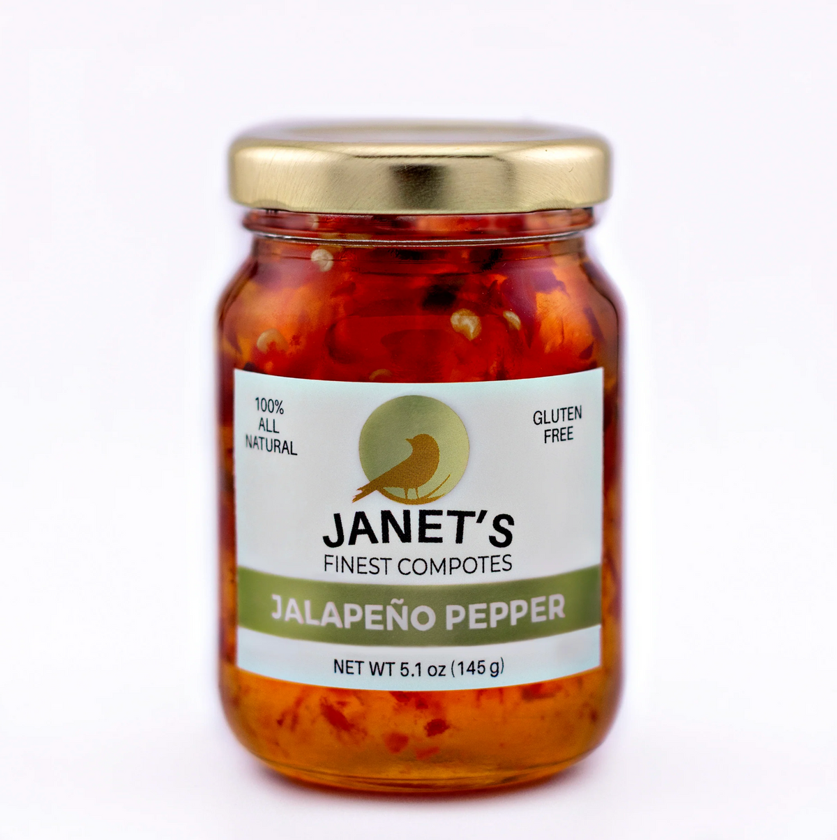 A glass jar of Janet's Finest Compotes Jalapeño Pepper, featuring a white label with green accents and a gold metal lid, set against a plain white background.