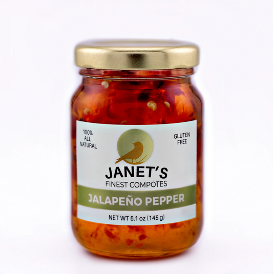 A glass jar of Janet's Finest Compotes Jalapeño Pepper, featuring a white label with green accents and a gold metal lid, set against a plain white background.