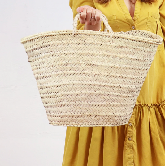 A woman in a long yellow dress holds a woven market basket tote bag with woven handles.