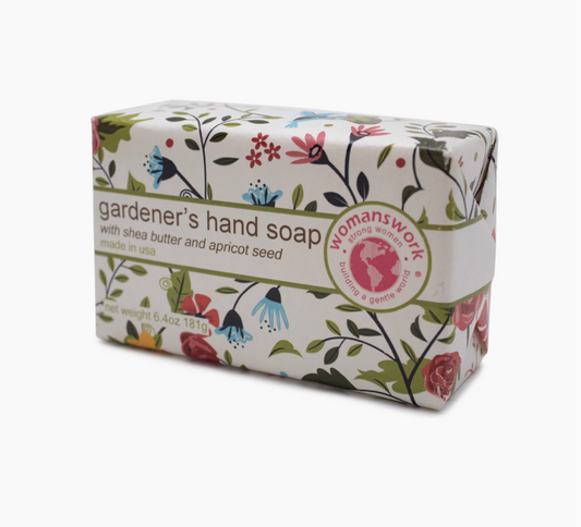 A rectangular bar of gardener's hand soap wrapped in a white paper sleeve with a colorful floral and bird pattern, featuring the 'Womanswork' brand logo on the side.