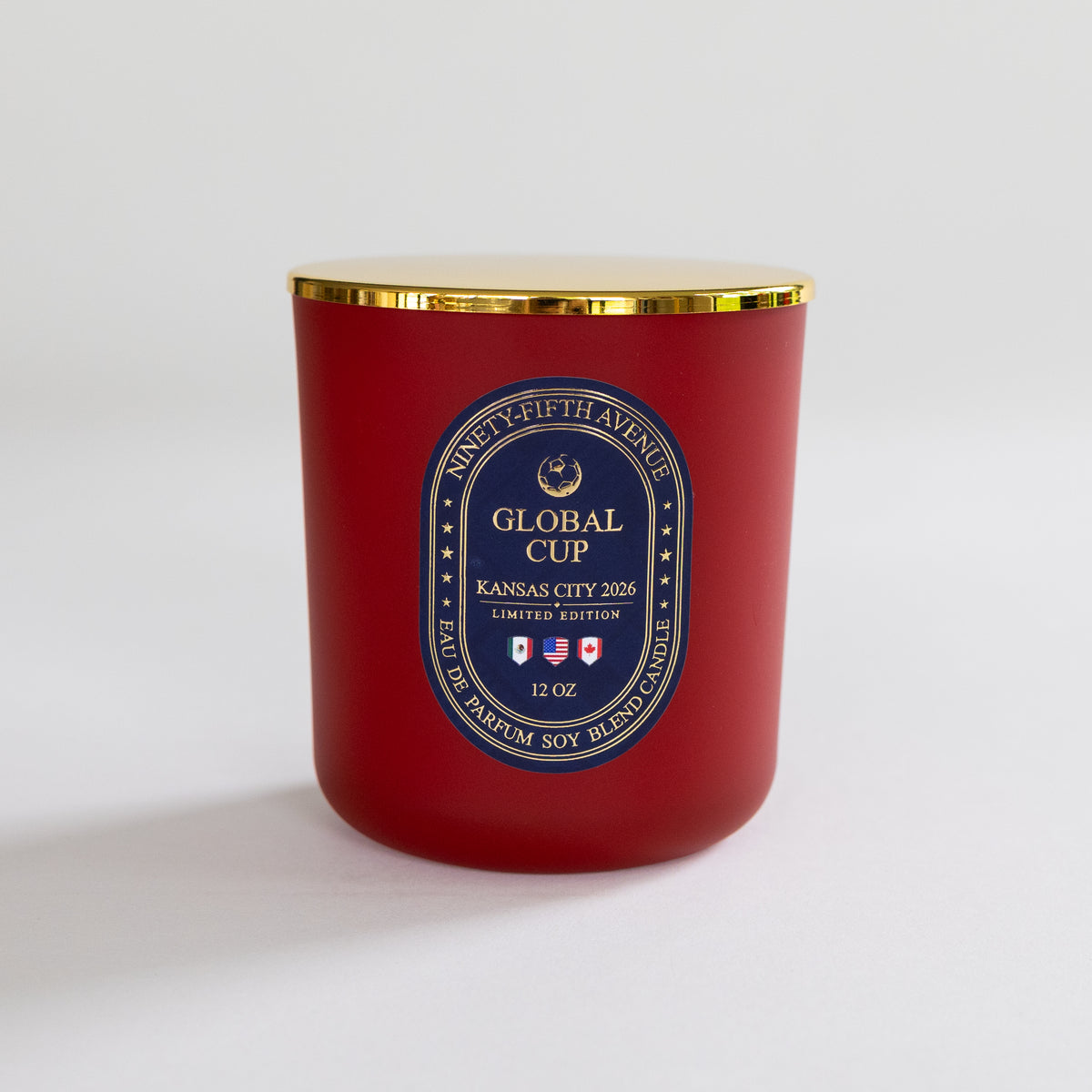 A red soy wax candle in a glass jar with a gold metal lid and a blue and gold circular label reading 'Global Cup Kansas City 2026'.