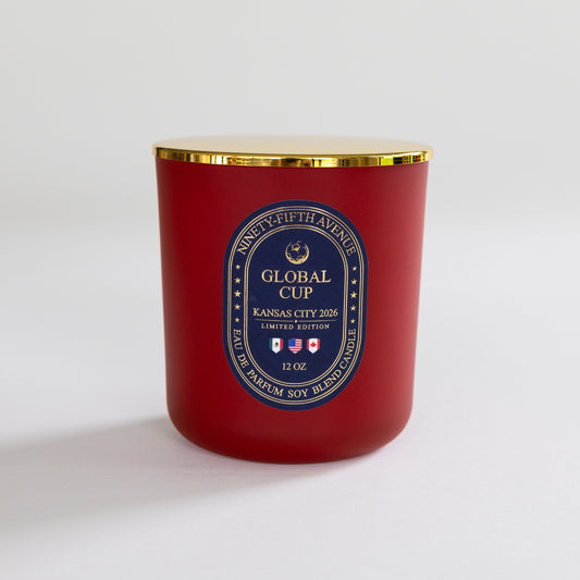 A red soy wax candle in a glass jar with a gold metal lid and a blue and gold circular label reading 'Global Cup Kansas City 2026'.