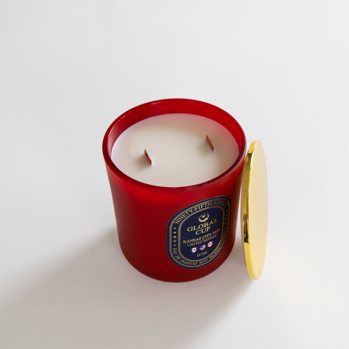 A red glass jar candle with white wax and two wicks, shown with its gold-toned lid leaning against it on a clean white background. The front label reads 'Global Cup' and 'Scented Candles'.