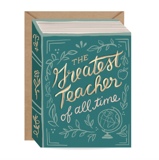 A book-style greeting card with a kraft envelope behind it. The card has a teal cover with white line-art illustrations of leaves, apples, and a globe, plus large gold script text reading 'The Greatest Teacher of all time.