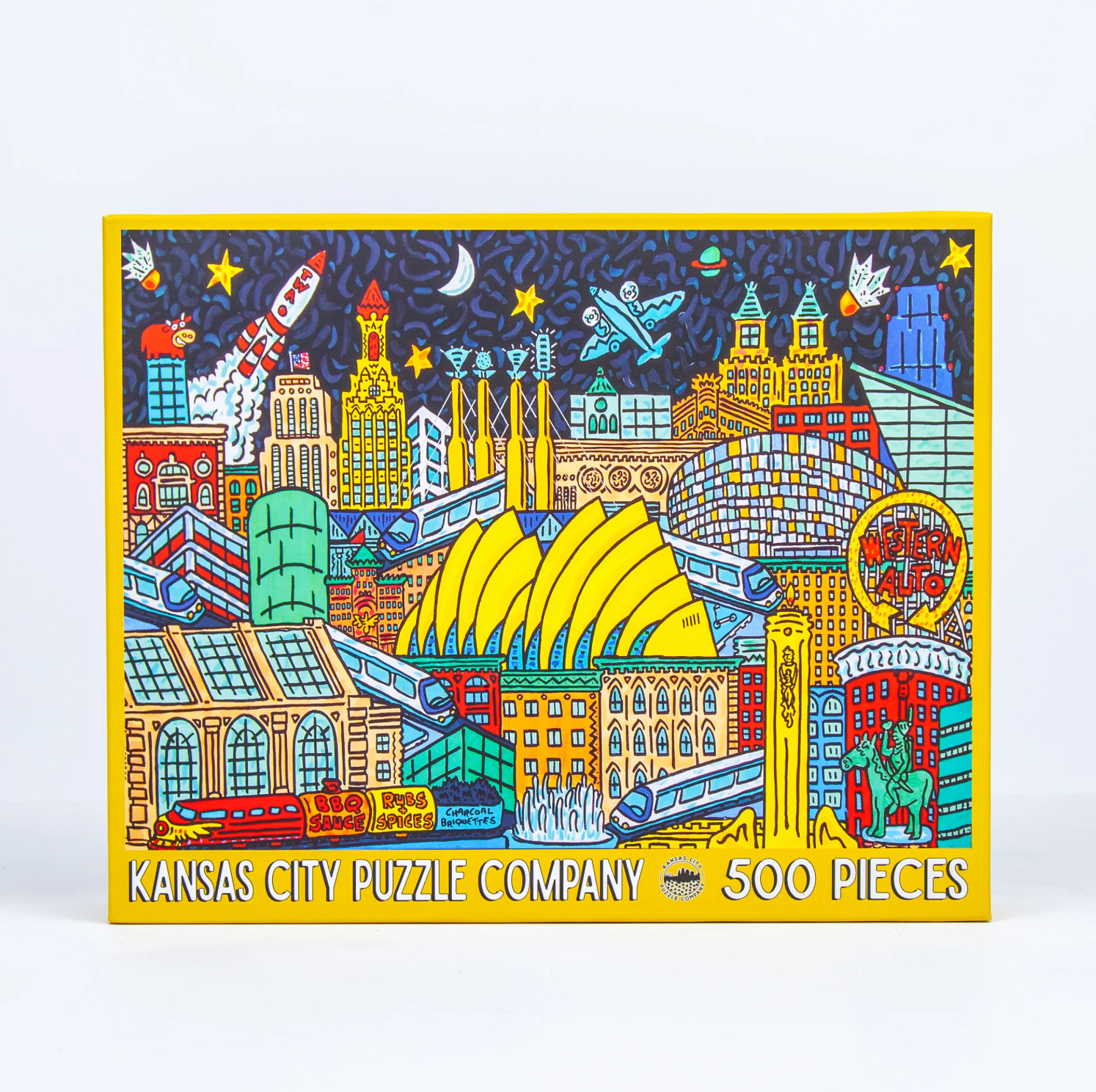 Kansas City Puzzle Company 500-piece jigsaw puzzle box featuring a colorful illustrated skyline of Kansas City with buildings, trains, a rocket, and a moon against a dark blue sky.
