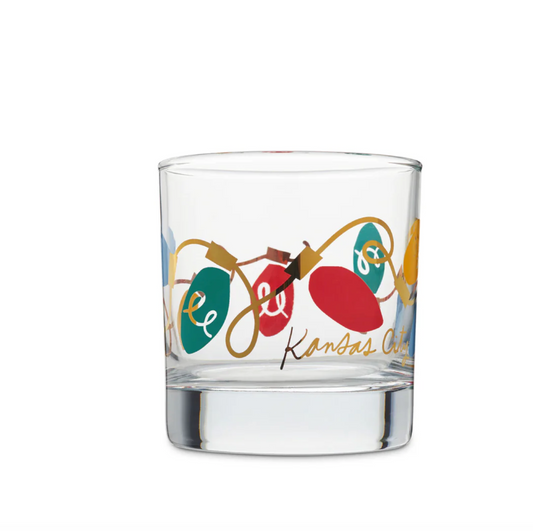 A clear glass rocks tumbler featuring a festive Christmas string lights design with red, green, and gold holiday bulbs and the text 'Kansas City' in gold script.